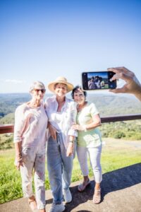 A group of elderly women on a mountaintop taking a selfie during their Sunshine Coast tour.