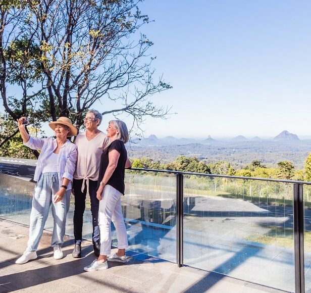 Three women taking a picture on a balcony overlooking the mountains during a sunshine coast day trip.