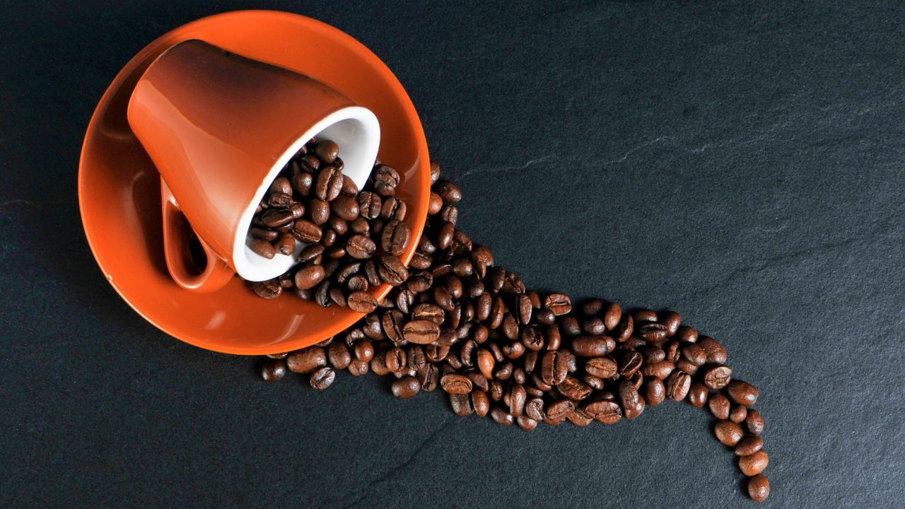 A cup of coffee and coffee beans on a black background, perfect for sunshine coast sightseeing and noosa tours.