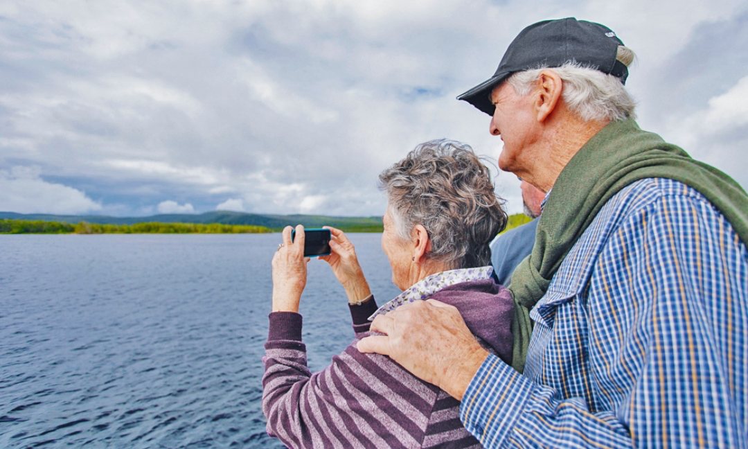 An older couple enjoying a sunshine coast day trip, capturing a picture of a serene lake during their noosa tour.