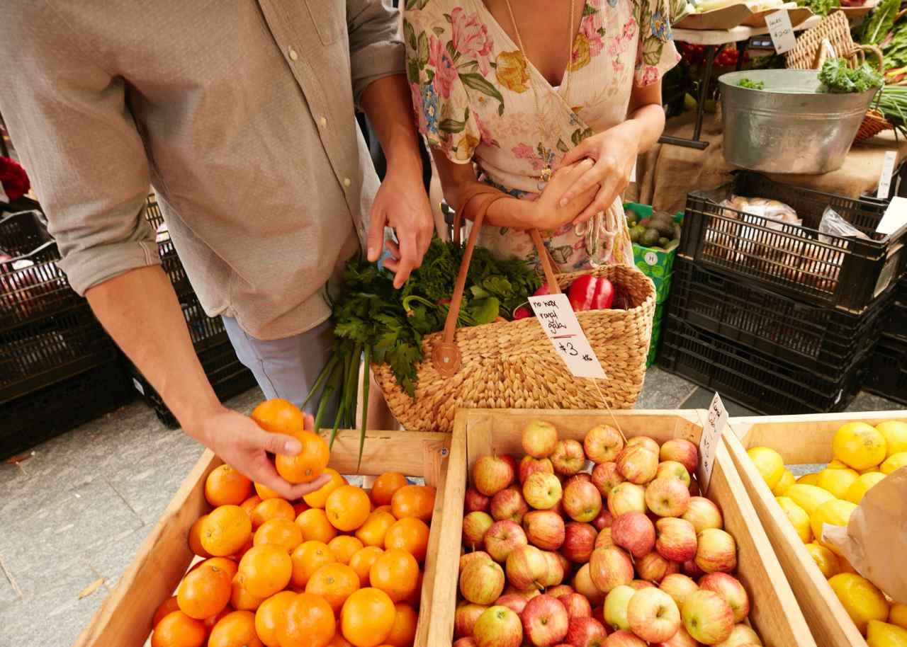 A couple is shopping at a farmers' market on a sunshine coast day trip.