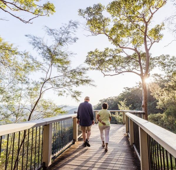 An older couple enjoying a leisurely stroll on a picturesque bridge amidst the lush greenery of the forest.