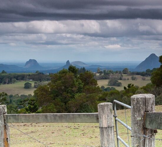 A fence with a view of mountains and a cloudy sky, perfect for Sunshine Coast sightseeing.