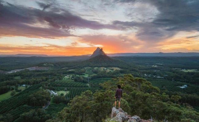 A man enjoying the breathtaking sunset view from atop a mountain on the Sunshine Coast.