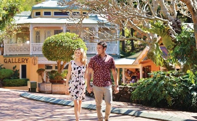 A man and woman enjoying a Sunshine Coast wine tour, walking down a street in a charming town.