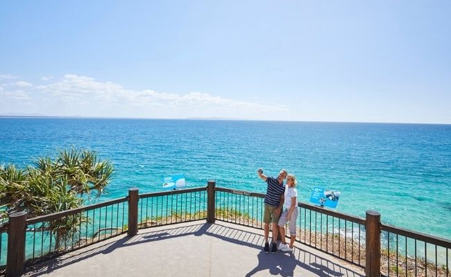 Two people standing on a railing overlooking the ocean during a Sunshine Coast sightseeing tour.