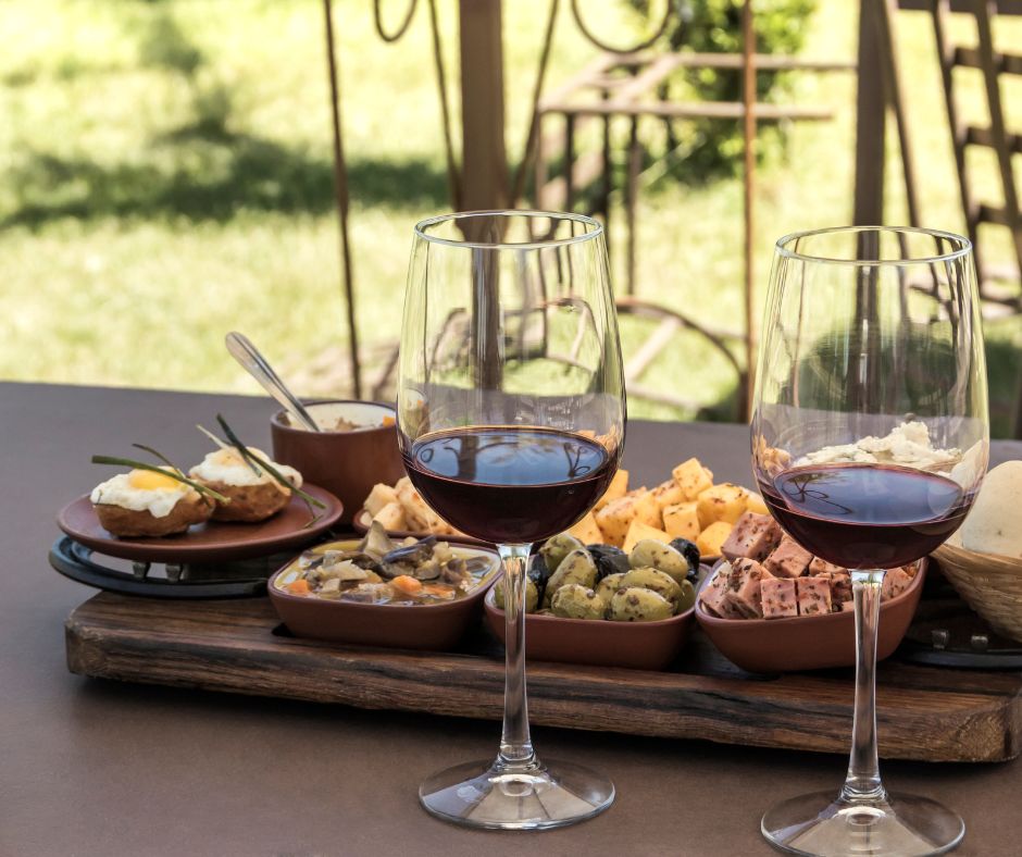 A delightful spread of food and two glasses of wine are beautifully presented on a rustic wooden tray during a Maleny wine tour.
