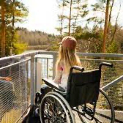 A girl in a wheelchair enjoying the sunshine coast views from a bridge overlooking a picturesque lake.