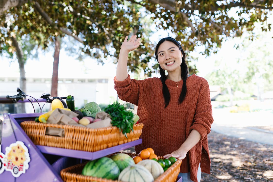 A woman is standing next to a purple cart full of fruits and vegetables on the Sunshine Coast.