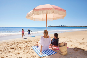 two people sitting under a pink umbrella on the beach