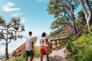 Two people walking down a path with surfboards on a sunshine coast sightseeing adventure.