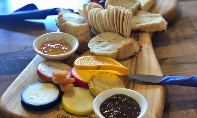 A wooden board with fruit, bread and cheese on it,