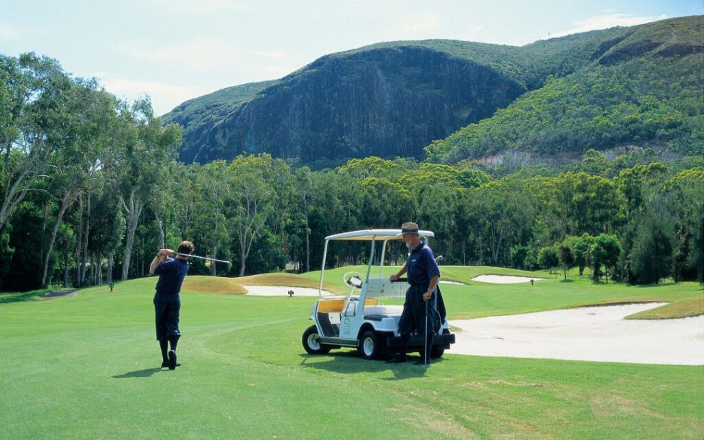 Two golf carts on a golf course with mountains in the background.