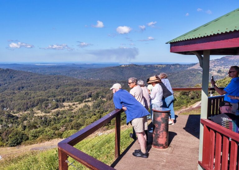 Tourists enjoying a scenic view from a mountain lookout on their Montville Day Tour with a clear blue sky in the background. Sunshine Coast Hinterland Highlights Tour: Discover Maleny and Montville
