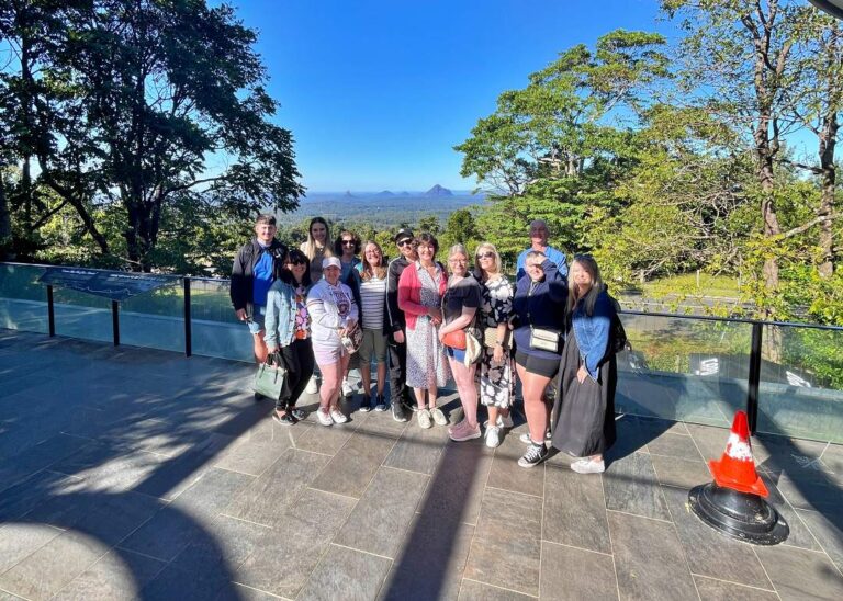 Group of tourists posing for a photo with a scenic natural backdrop and clear blue skies during their Montville Day Tour. Sunshine Coast Hinterland Highlights Tour: Discover Maleny and Montville