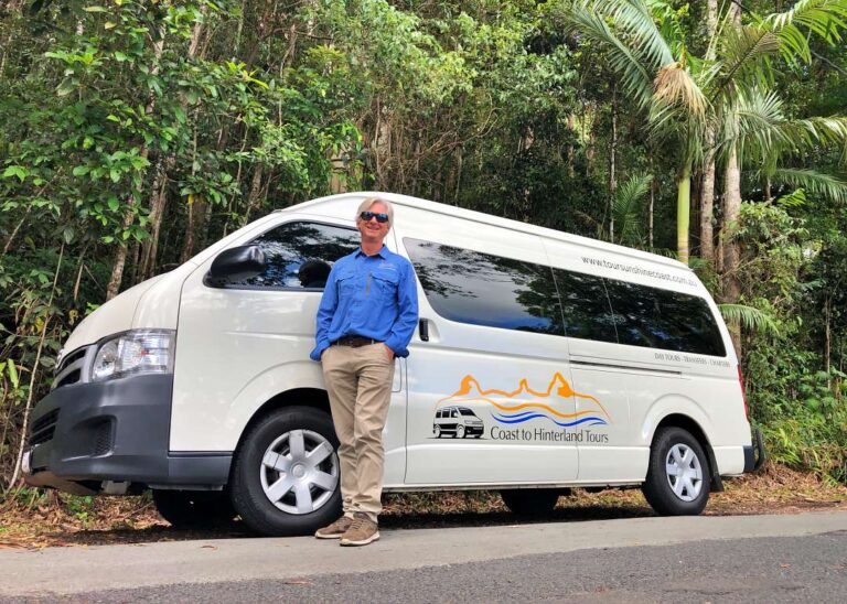 Tour guide standing next to a minibus for Montville Day Tour from coast to hinterland tours. Sunshine Coast Hinterland Highlights Tour: Discover Maleny and Montville
