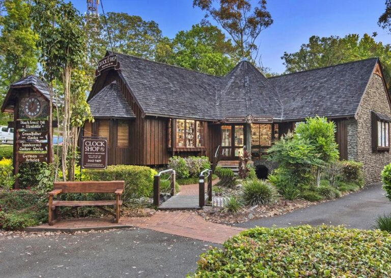 Charming Montville Day Tour clock shop nestled in a lush garden setting with a rustic wooden bench out front. Sunshine Coast Hinterland Highlights Tour: Discover Maleny and Montville